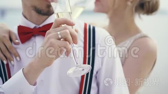 特写镜头，新婚夫妇在露天喝香槟，穿着吊带和红色领结的时髦年轻新郎，金发新娘