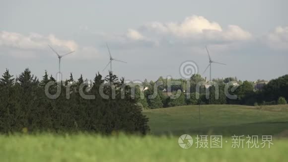 旋转风力涡轮机在远处被树木和草包围。 乡村的旋转风车被