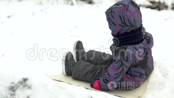 一个孩子在雪地滑梯上翻滚。 冬天在街上玩。 在寒冷的冬天，孩子穿着一件夹克和一件