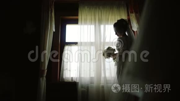 新娘穿着白色丝绸礼服，在木房子的全景窗旁停留