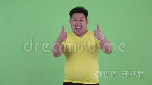 快乐的年轻超重的亚洲男人竖起大拇指，看上去很兴奋