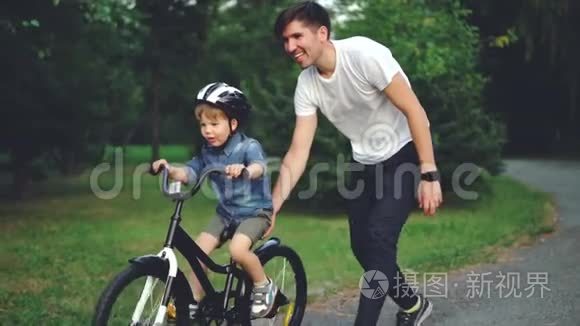 带着细心的父亲在公园里骑自行车，笑孩子骑自行车的慢动作。 年轻快乐