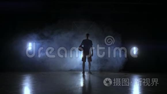 一个篮球运动员在黑暗的背景上的剪影，在篮球场上冒烟，抛出一个篮子球，