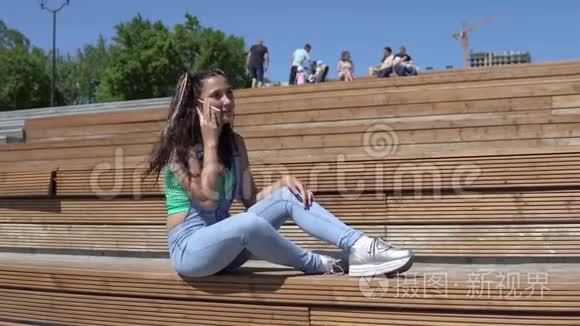坐在公园长凳上用手机说话的女孩。 4K