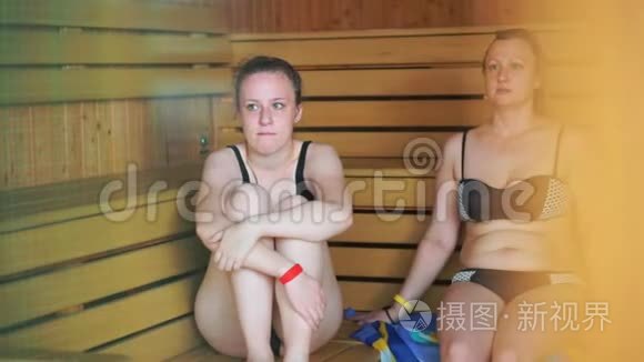 穿着泳衣的女儿和母亲坐在公共桑拿浴室的架子上。