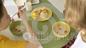 男孩在盘子里倒牛奶和玉米片，两个兄弟在吃早餐