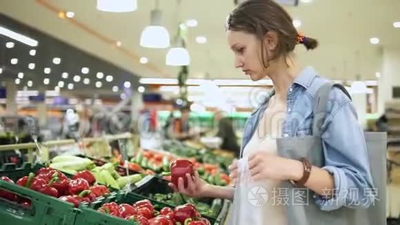 购物。 在蔬菜商店或超市选择生物红铃椒的女人。 一个接一个地把它放进