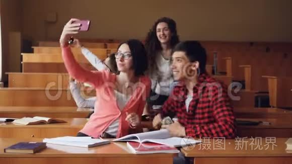快乐的学生正在教室里自拍，坐在桌子旁，拿着智能手机。 现代技术