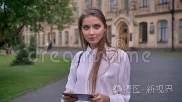 年轻迷人的女学生在夏天手里拿着平板电脑，看着镜头，交流理念