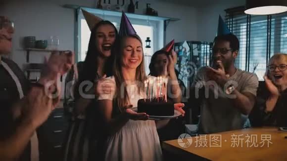 快乐的欧洲女孩拿着生日蛋糕，许愿吹着，多民族朋友在欢乐的聚会上唱着慢动作。