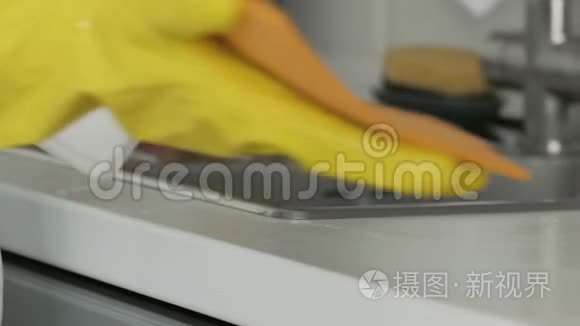 家庭主妇戴黄色手套用橙色抹布和洗涤剂洗桌子。