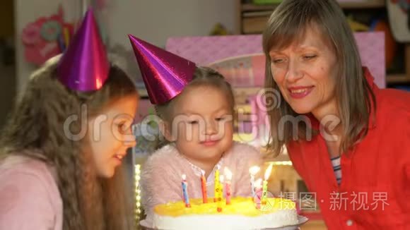 中年妇女和她的孙女戴着派对帽，送蛋糕和吹蜡烛
