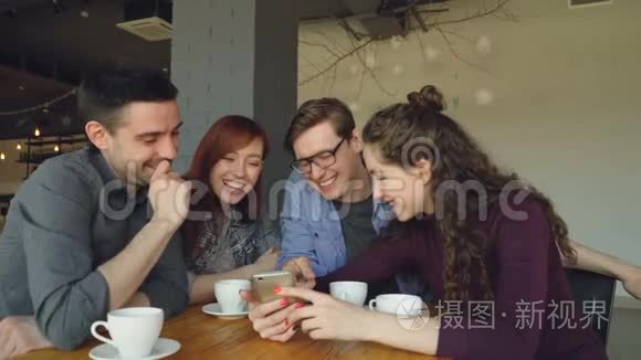 年轻人正在看智能手机屏幕，讨论照片，并在咖啡厅午休时大笑。 友谊